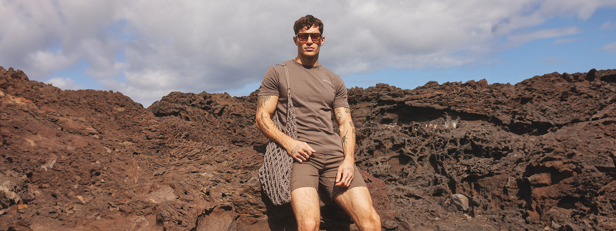 SikSilk model sat on the rocks, in the sun, modelling new T-shirt & Shorts
