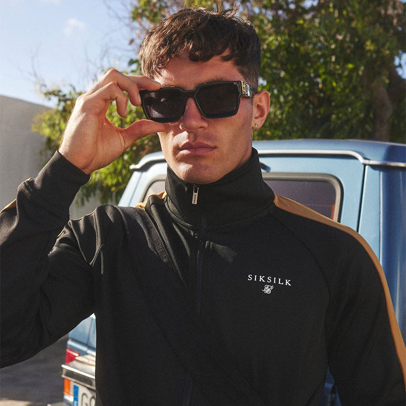 Model posing in Black & Gold SikSilk Track Top, with sunglasses.