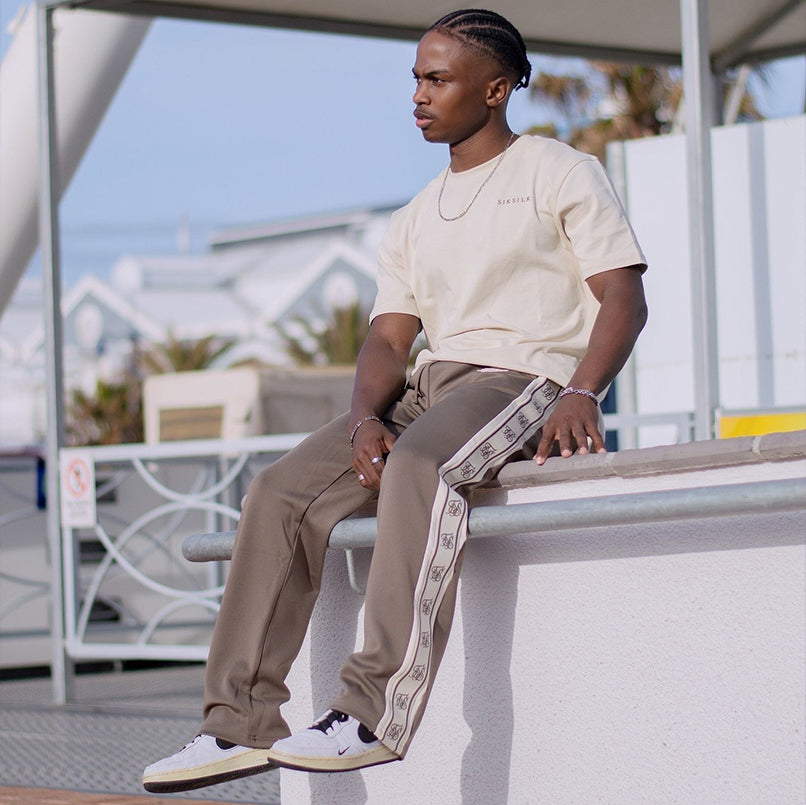 Model sat in the sun, wearing SikSilk Ecru Graphic T-Shirt & Brown SikSilk Track Pants